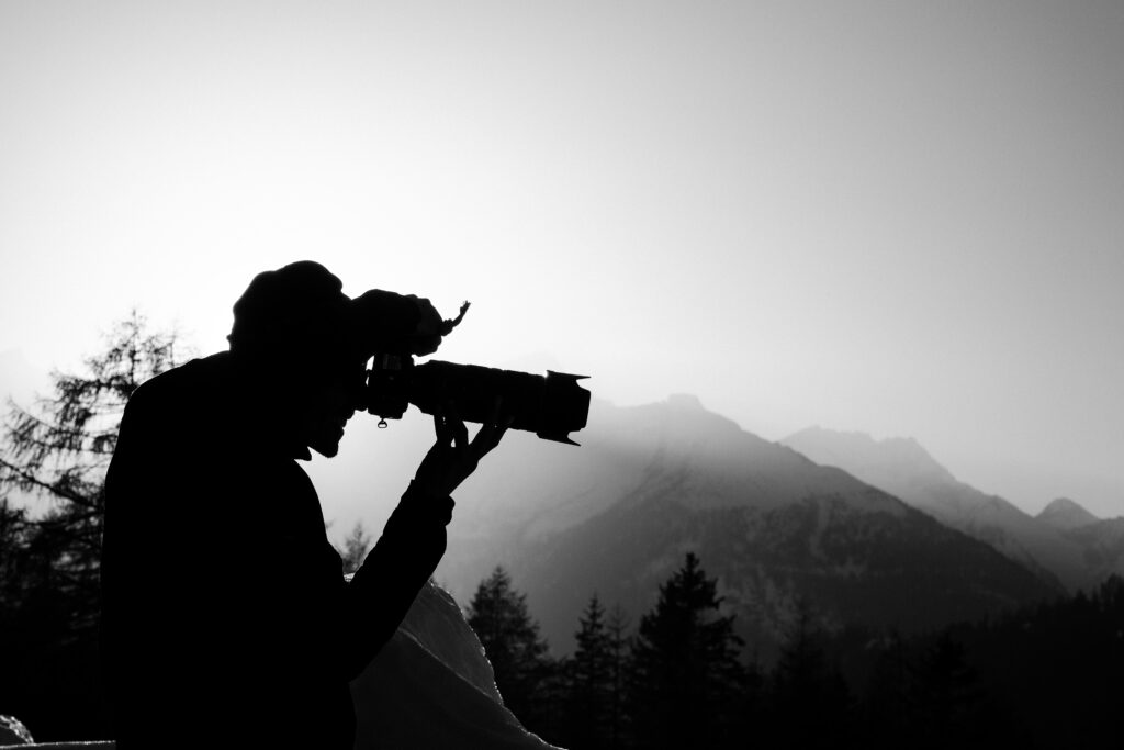 Schwarz-Weiß-Silhouette eines Fotografen mit Teleobjektiv vor Bergkulisse – klassische Bergfotografie