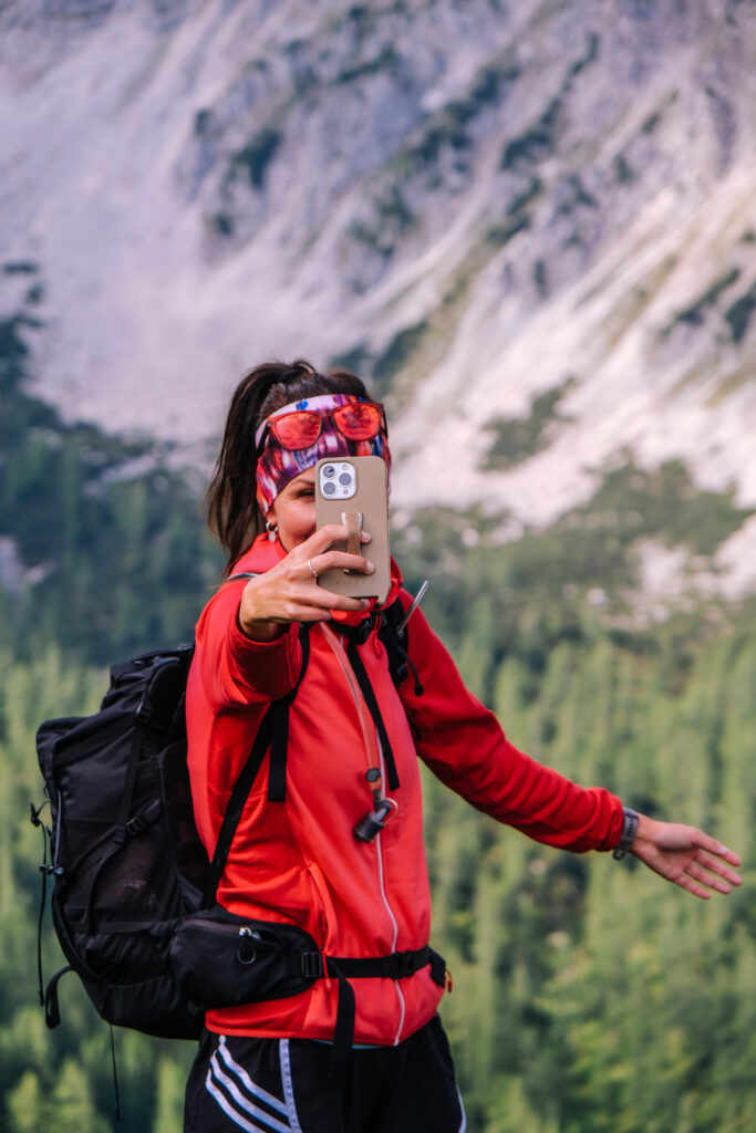 Wanderin in roter Jacke mit dem Smartphone vor Bergkulisse bei der Dümlerhütte