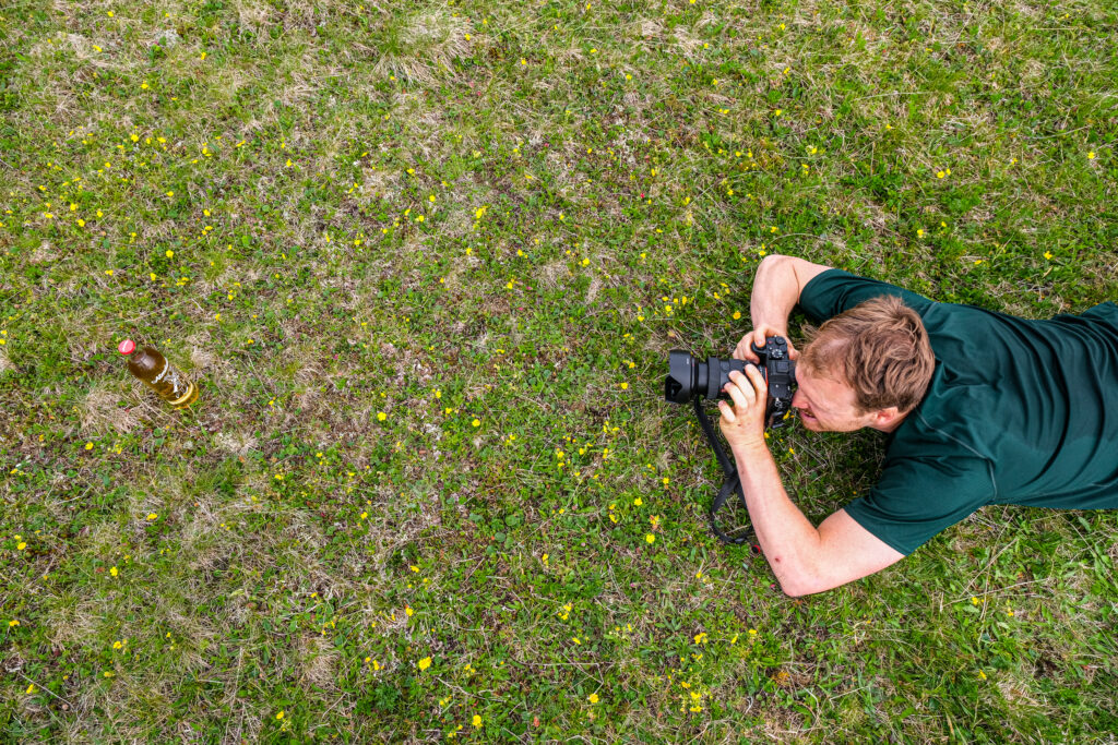 Fotograf liegt im Gras und fotografiert eine Blume aus nächster Nähe