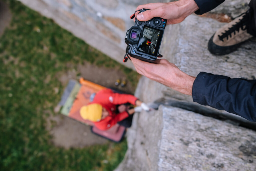 Fotograf kontrolliert am Wandkopf die Kamera, unten am Wandfuß ein Kletterer im Valle dell’Orco